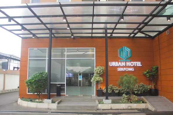 Un hotel urbano con fachada moderna, un amplio acceso de vidrio y un logotipo con una 'U' y una 'H' estilizadas.