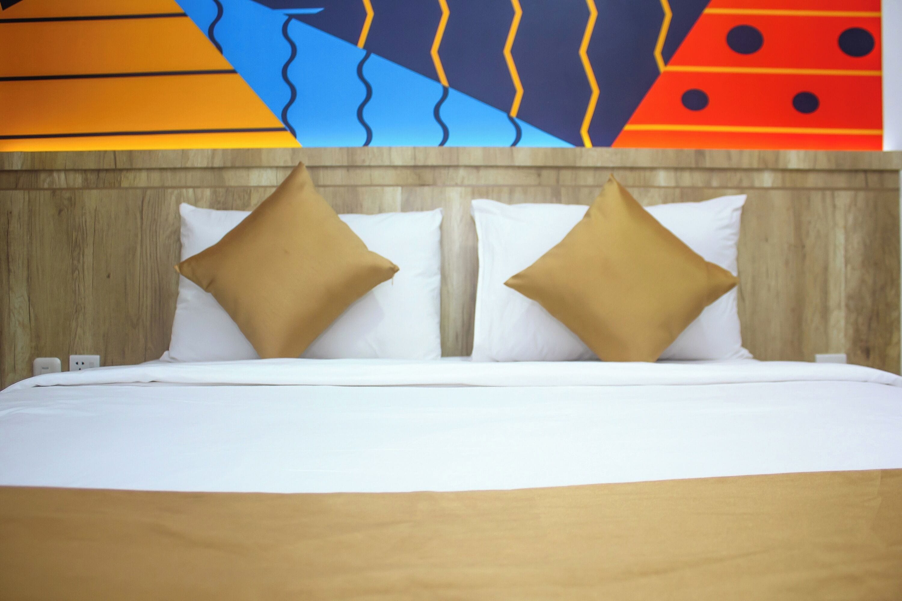 A bed with white and beige bedding, two pillows, and a wooden headboard.