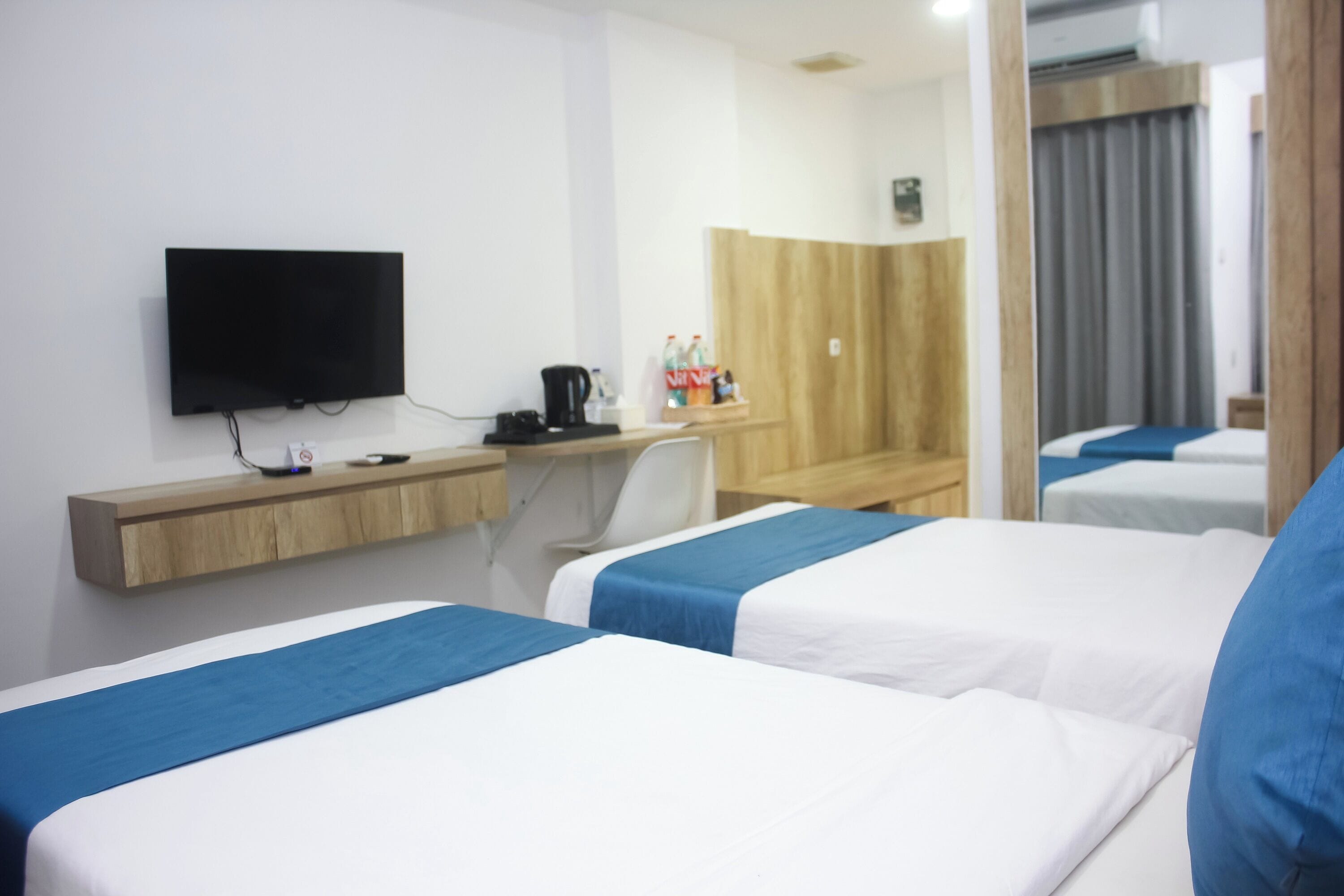 A hotel room with two beds, a desk, a television, and a mirror.