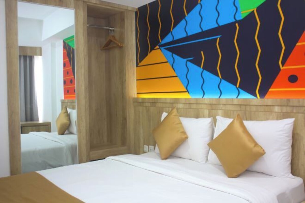 A hotel room with a bed, a wooden headboard, and a colorful abstract painting on the wall.