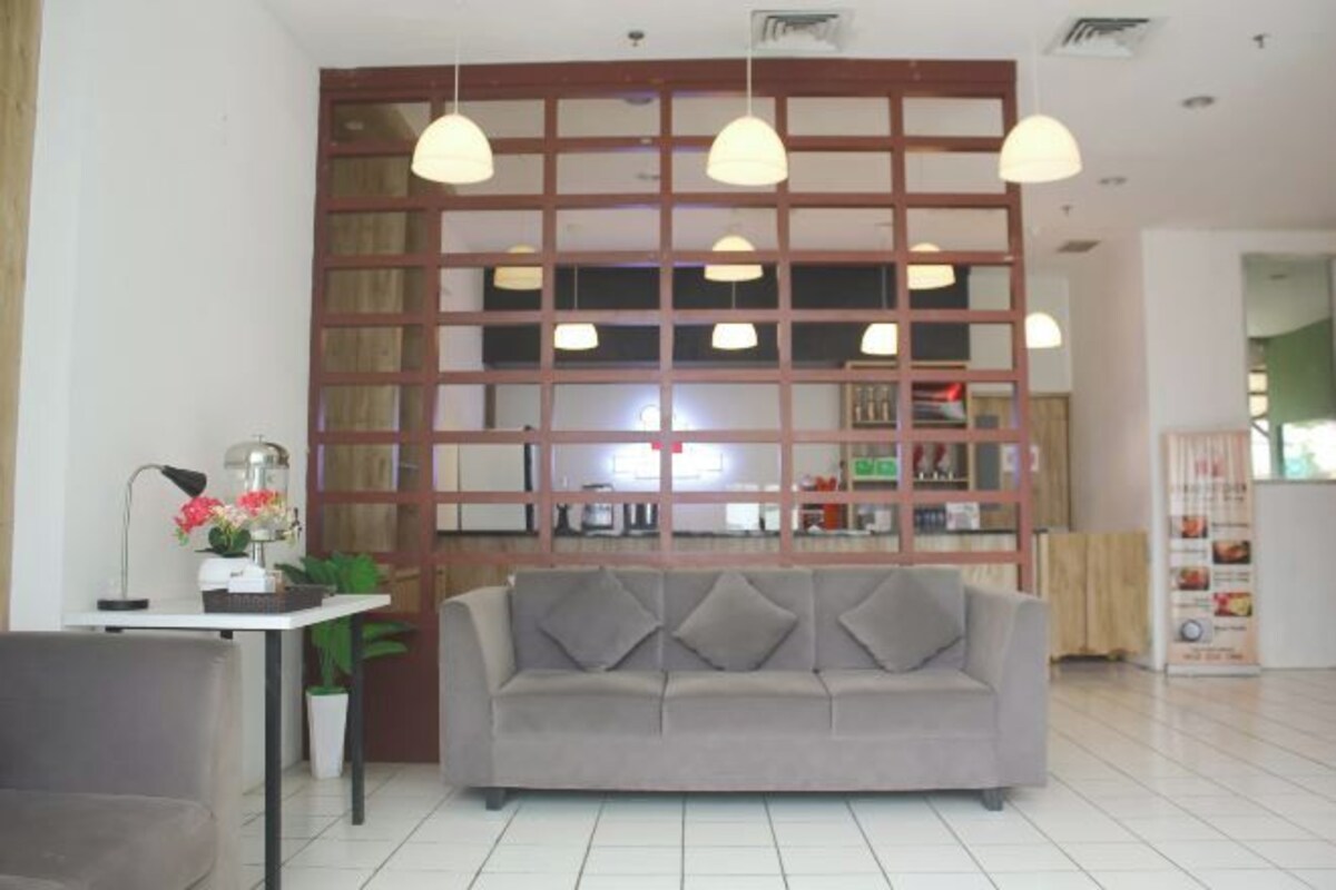 A modern living room with a grey sofa, a white coffee table, and a desk with a lamp. There is a wooden partition with a grid of windows behind the sofa.