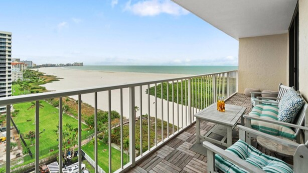 A balcony with a view of a beach, a table with chairs, and a small garden area. - Stunning Southern Beach Views the Whole Family will Love; Heated Pool & WiFi ~Walk to Dining & Shops (Marco Island)