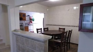 A kitchen with a central island, wooden dining table, and chairs. There is a window with a view of the outside.