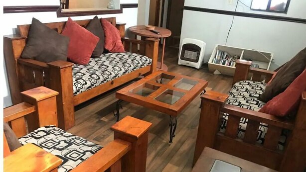 A cozy living room with wooden furniture, including a sofa and a coffee table with glass panels.