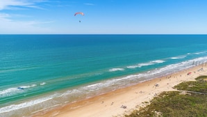 A beach with a clear view of the ocean, a person paragliding, and a sandy shore with people and umbrellas. - Bayfront Condo With Water View & Boat Slips! (South Padre Island)
