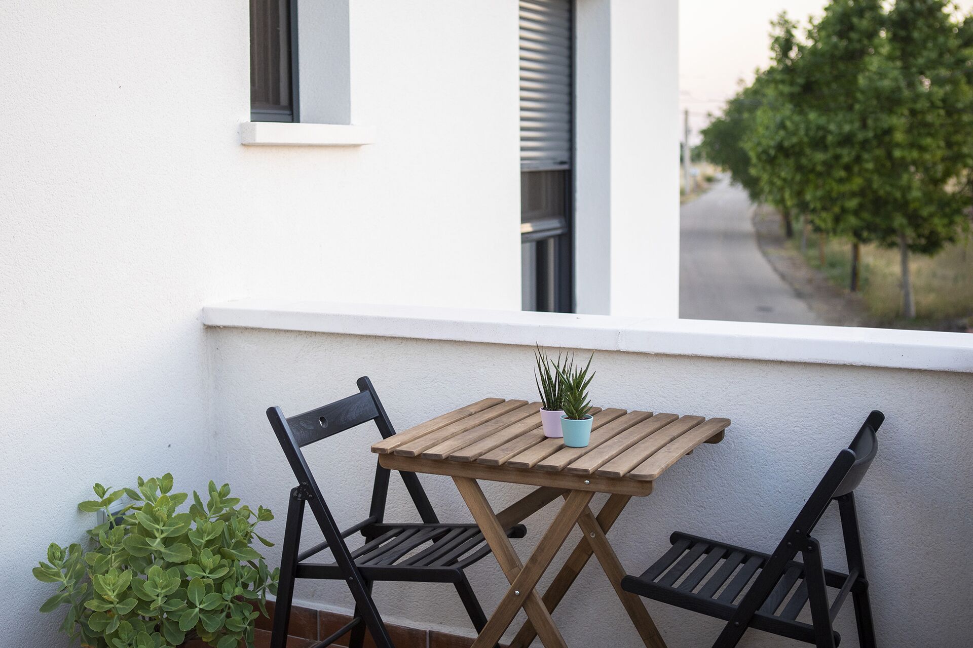 Une table en bois et deux chaises sur un balcon, avec un pot de fleurs.