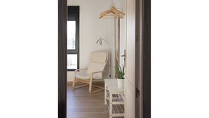 Una stanza con pavimento in legno, una sedia bianca, una scrivania con una pianta e un appendiabiti.