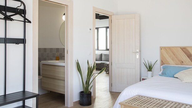 Una camera da letto con un letto, una testiera in legno, un comodino, una lampada a sospensione e vista sul bagno.
