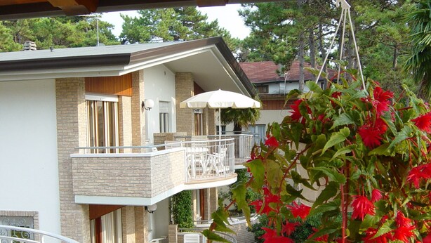 Ein zweistöckiges Gebäude mit Balkon, Sitzgelegenheiten im Freien und einem hängenden Blumentopf.