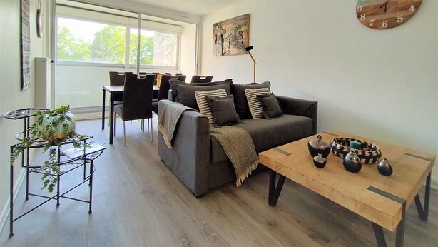 Ein modernes Wohnzimmer mit einem grauen Sofa, einem Holztisch und einem Essbereich mit Tisch und Stühlen.