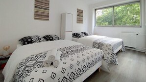 Ein Schlafzimmer mit zwei Betten, einem Muster-Bettwäsche, einem weißen Kleiderschrank und einem Fenster mit Blick auf Bäume.