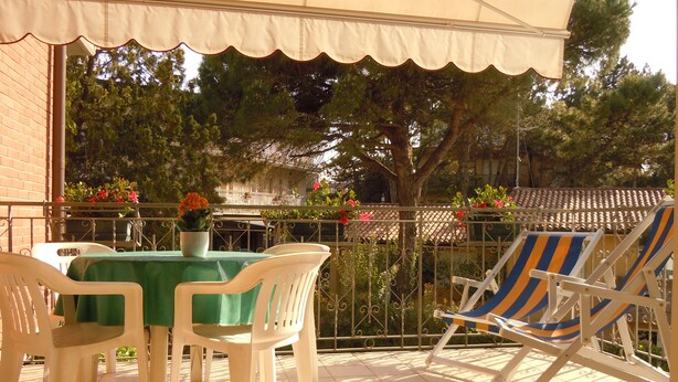 Un patio con tavolo e sedie, una zona coperta e un parapetto addornato con piante in vaso.