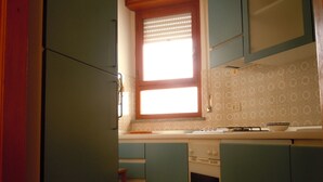 Una cucina compatta con mobili color acquamarina, una finestra con persiane, un piano cottura e un lavello.