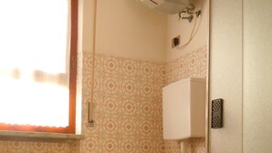 Un bagno con due servizi igienici, un lavandino, un termosifone e una finestra con tenda.