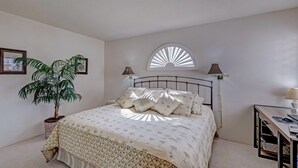 A bedroom with a bed, a potted plant, a desk, and a window with a sunburst design. - 2 bedroom spacious Condo (Palm Desert)