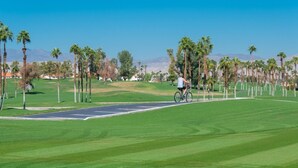 A golf course with a clear path, palm trees, and a cyclist. - 2 bedroom spacious Condo (Palm Desert)