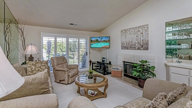 A living room with a sofa, armchair, coffee table, TV, fireplace, and a glass display cabinet. - 2 bedroom spacious Condo (Palm Desert)