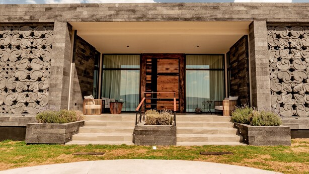 A modern building with a stone facade, a wooden door, and a set of steps leading to a covered entrance. - Hotel Boutique Tres Raíces (Dolores Hidalgo)