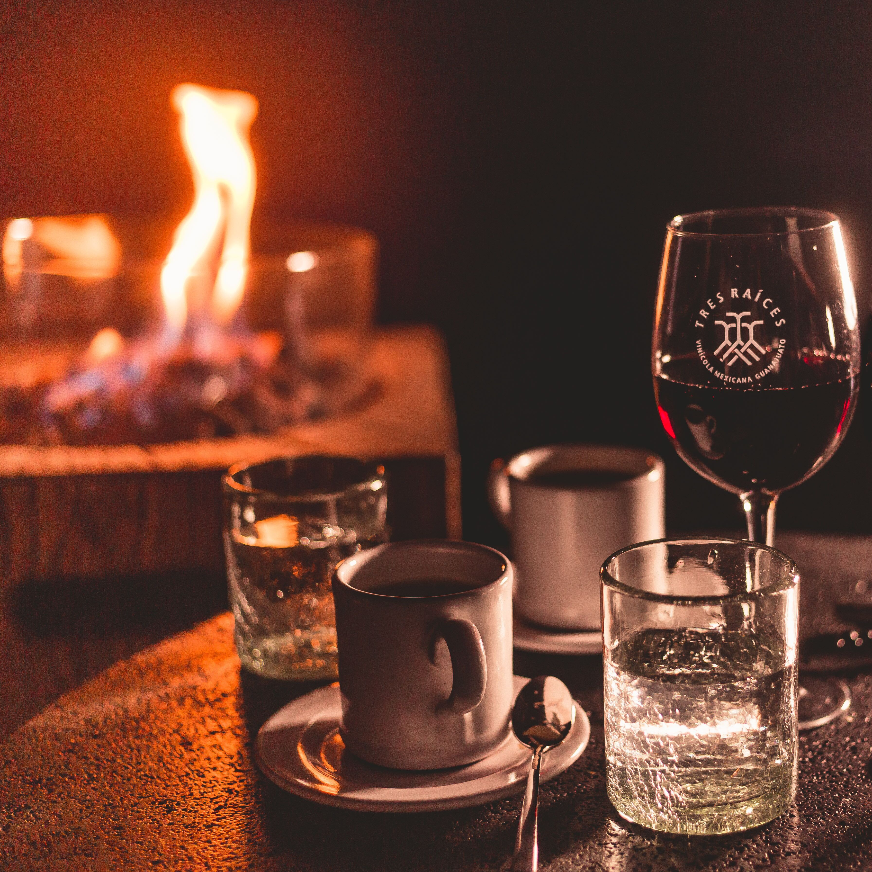 A table with a glass of red wine, a cup, and a glass of water, with a candle in the background.