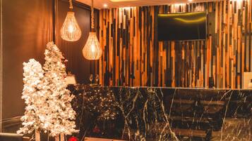 A modern lobby with a marble reception desk, two white Christmas trees, and a wooden wall with vertical slats.