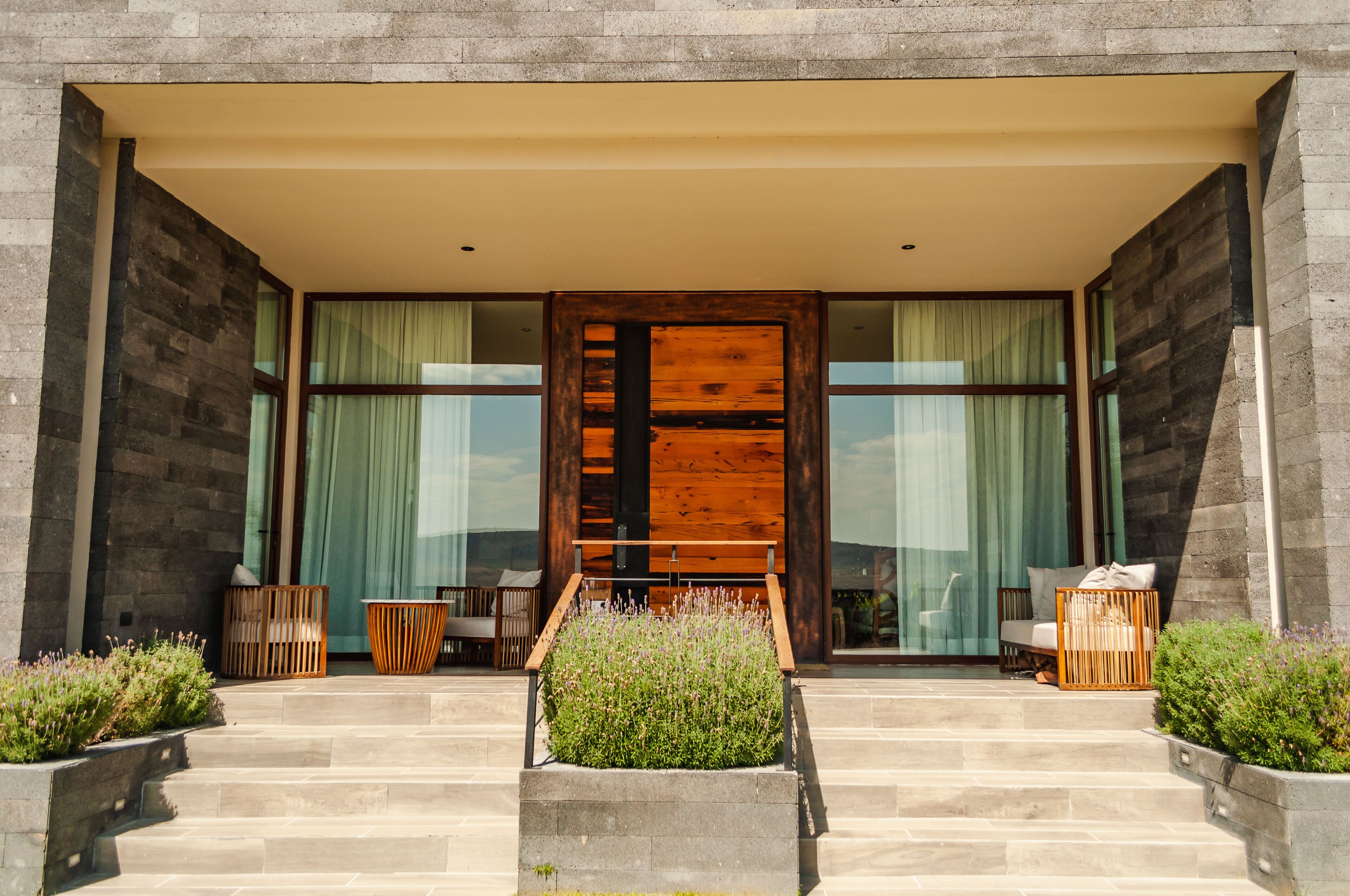 A modern building entrance with a wooden door, large windows, and outdoor seating.