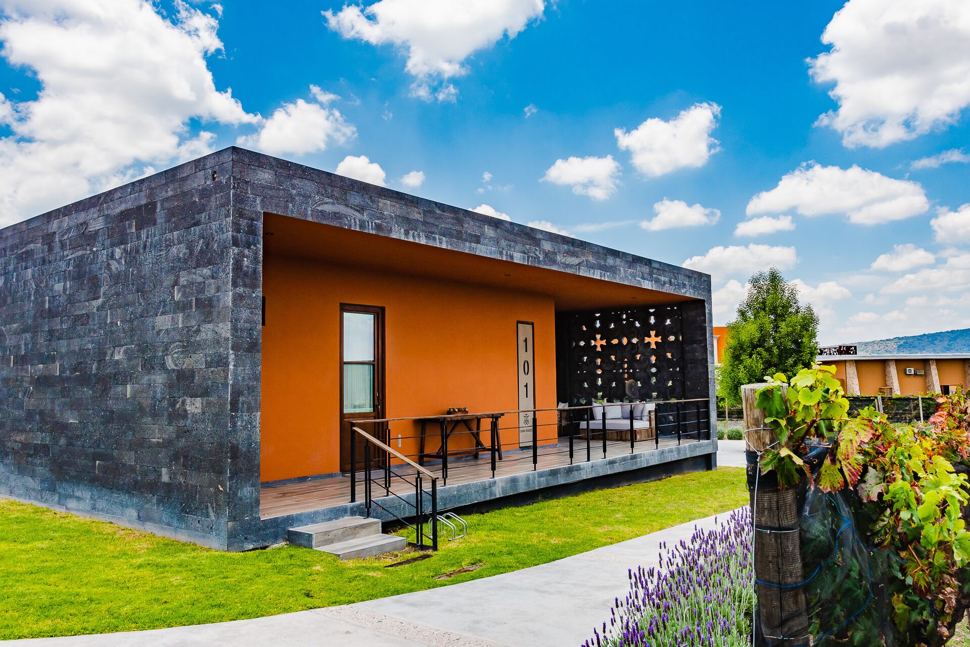 A modern building with a stone facade and an orange interior. It features a balcony with outdoor seating and a staircase leading to the entrance.