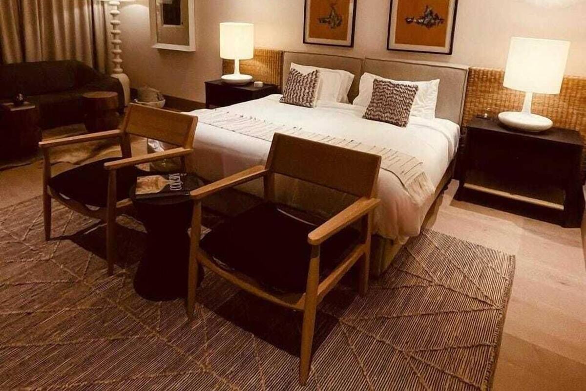A hotel room with a bed, two bedside tables, a chair, a desk, and a lamp.