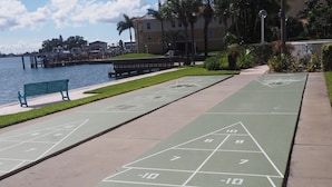 Een park met jeu de boules banen, een bankje en uitzicht op water en gebouwen.