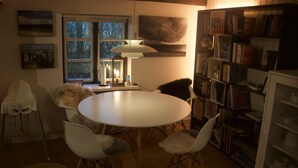 Ein gemütlicher Essbereich mit einem runden Tisch und weißen Stühlen, ein Bücherregal voller Bücher und ein Fenster mit Blick auf Bäume.