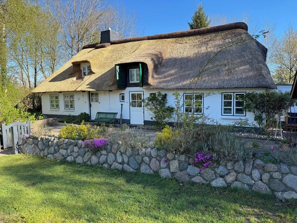 A traditional thatched-roof house with a stone wall and a bench in the front yard.