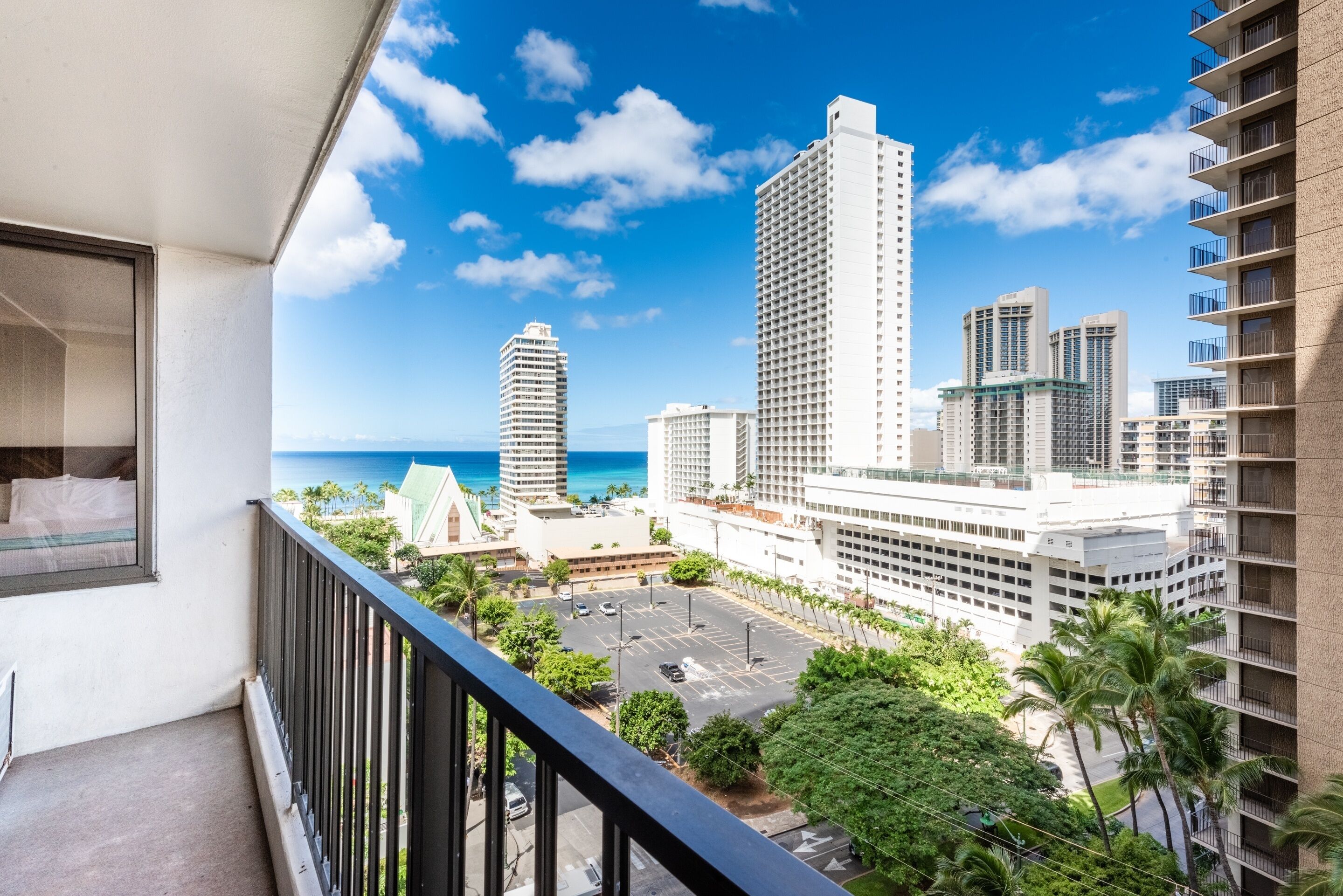 A balcony with a view of a cityscape, including tall buildings and a parking lot.