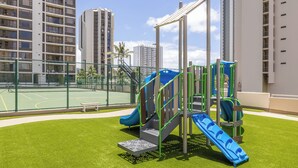 A playground with slides and climbing structures, surrounded by a fence and tall residential buildings. - Breezy Ocean View Waikiki Condo with Free Parking! (Honolulu)