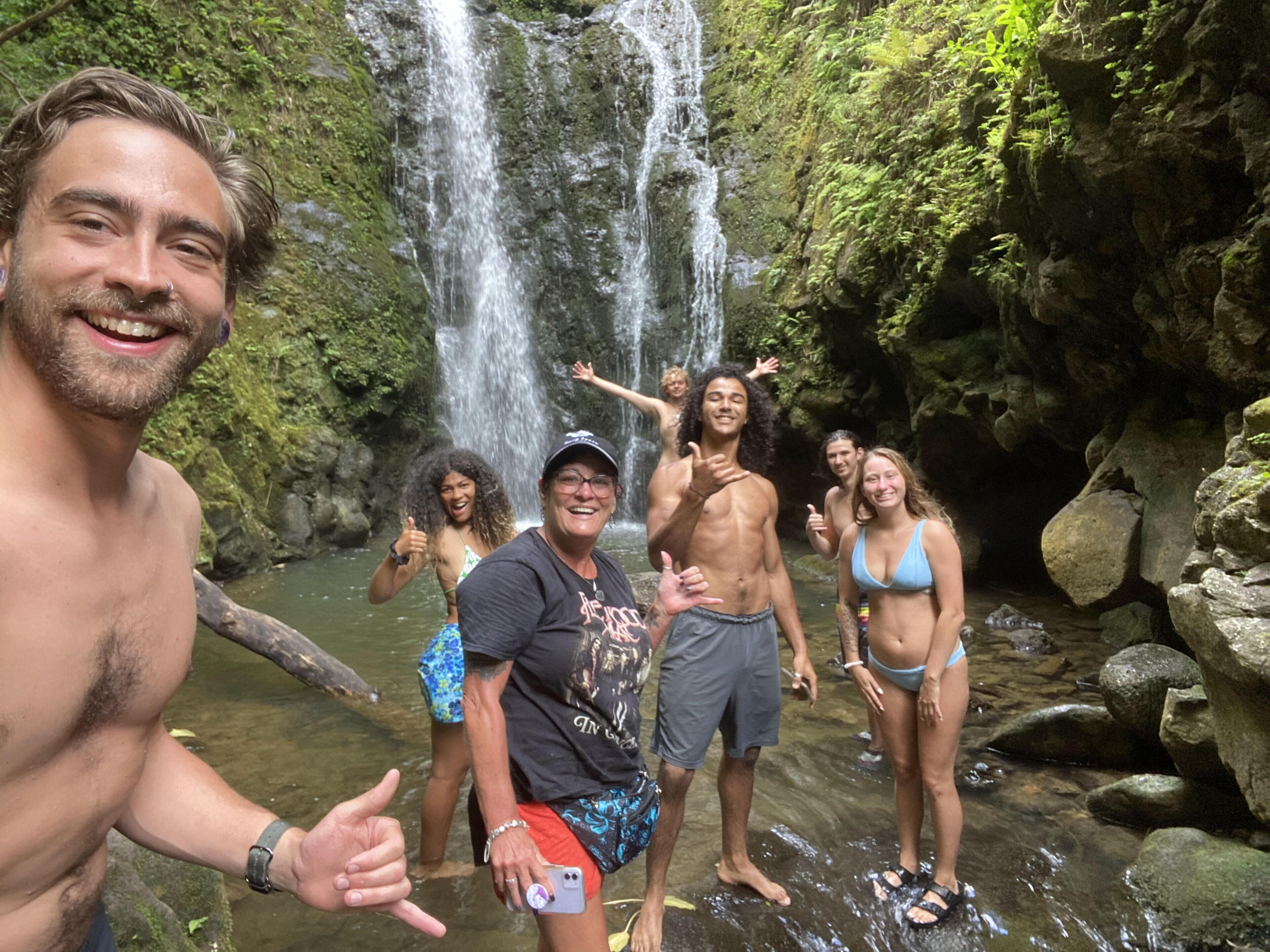 Un groupe de personnes se tient près d’une cascade, dans un cadre naturel.