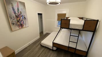 A bedroom with a bunk bed, a small table, a painting on the wall, and a window with blinds.