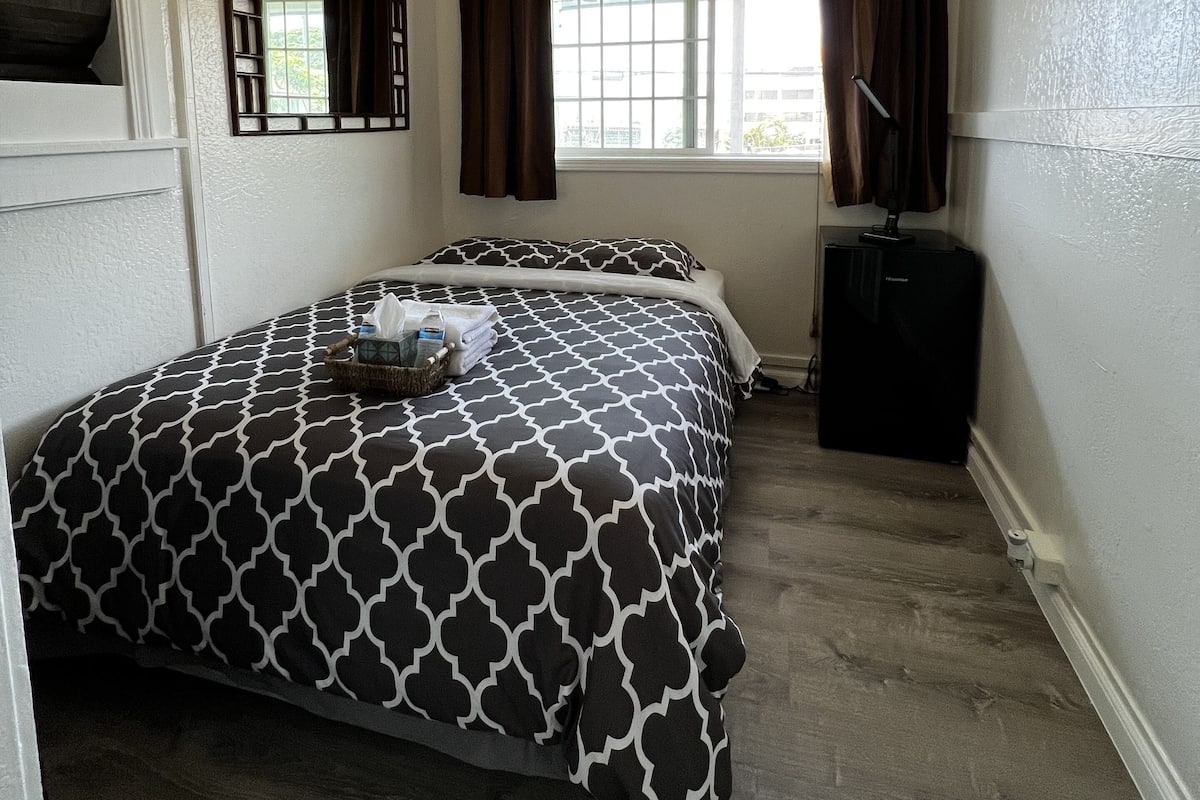 Une chambre à coucher comprenant un lit, un ventilateur de plafond, une fenêtre avec des rideaux, une commode et un miroir.