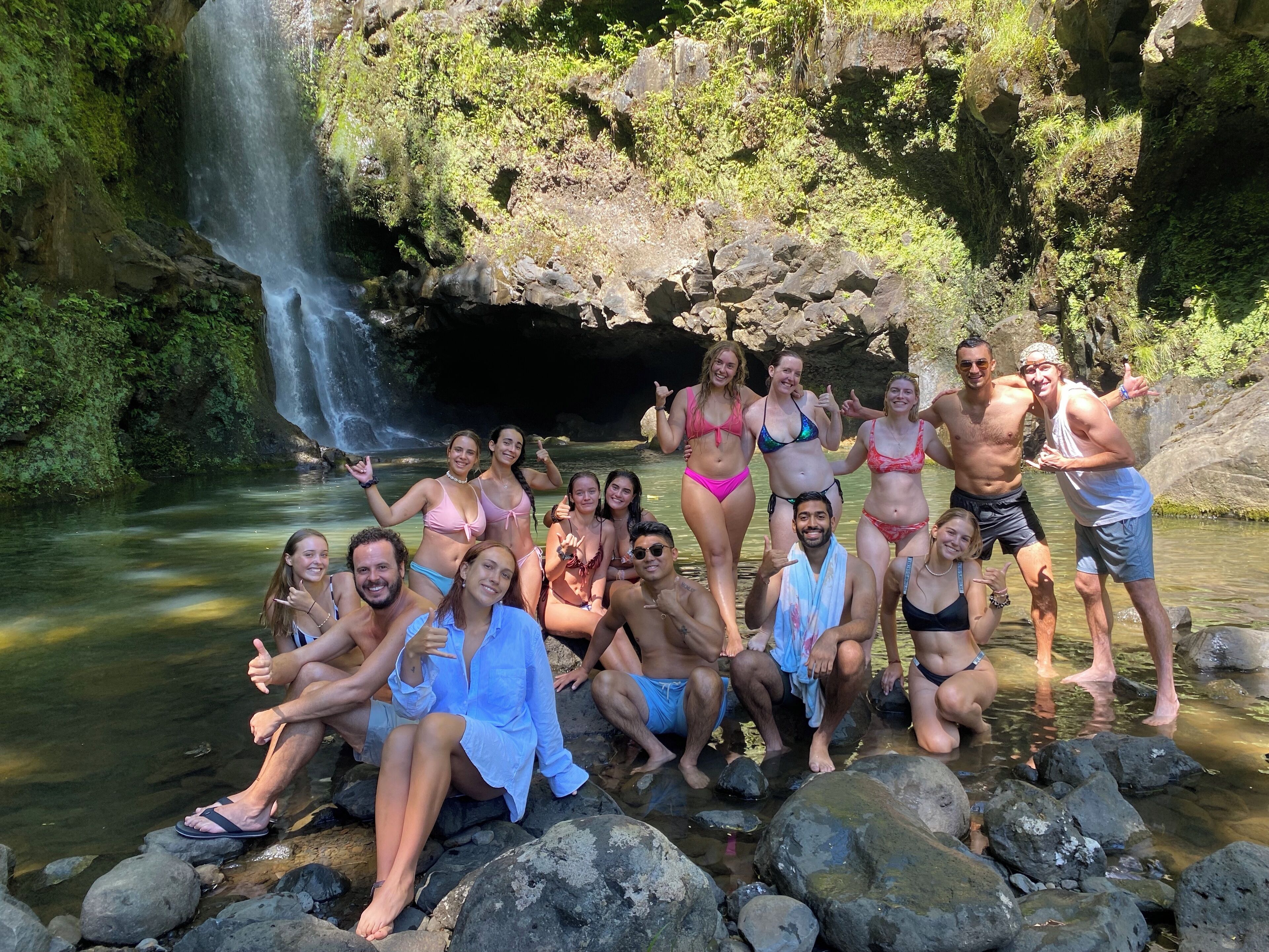 A group of people posing by a waterfall in a natural setting.