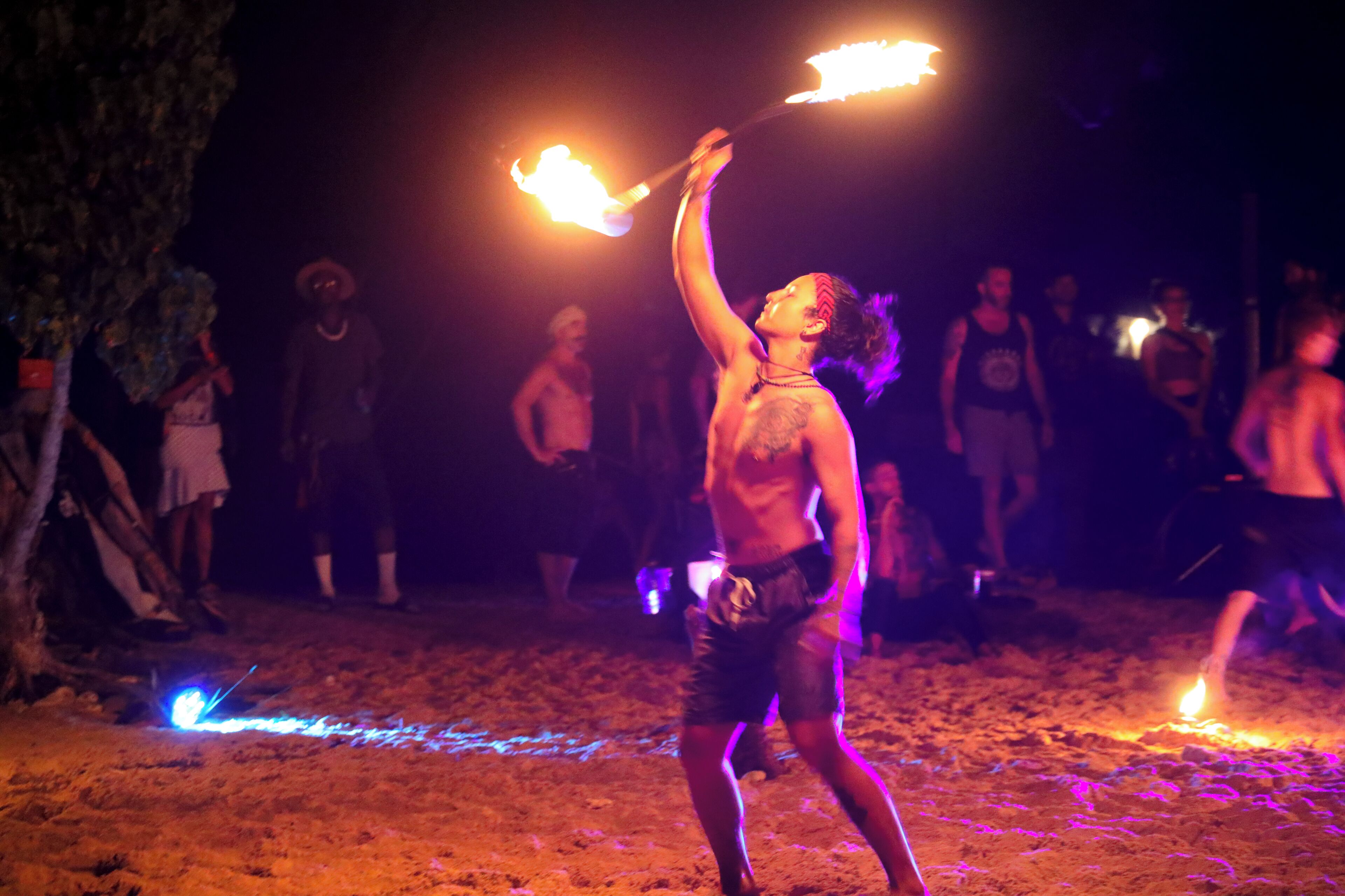 A person performing with fire props on a sandy surface, possibly at an outdoor event.