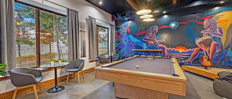 Una mesa de billar con un mural, sillas y vistas por ventanas amplias.