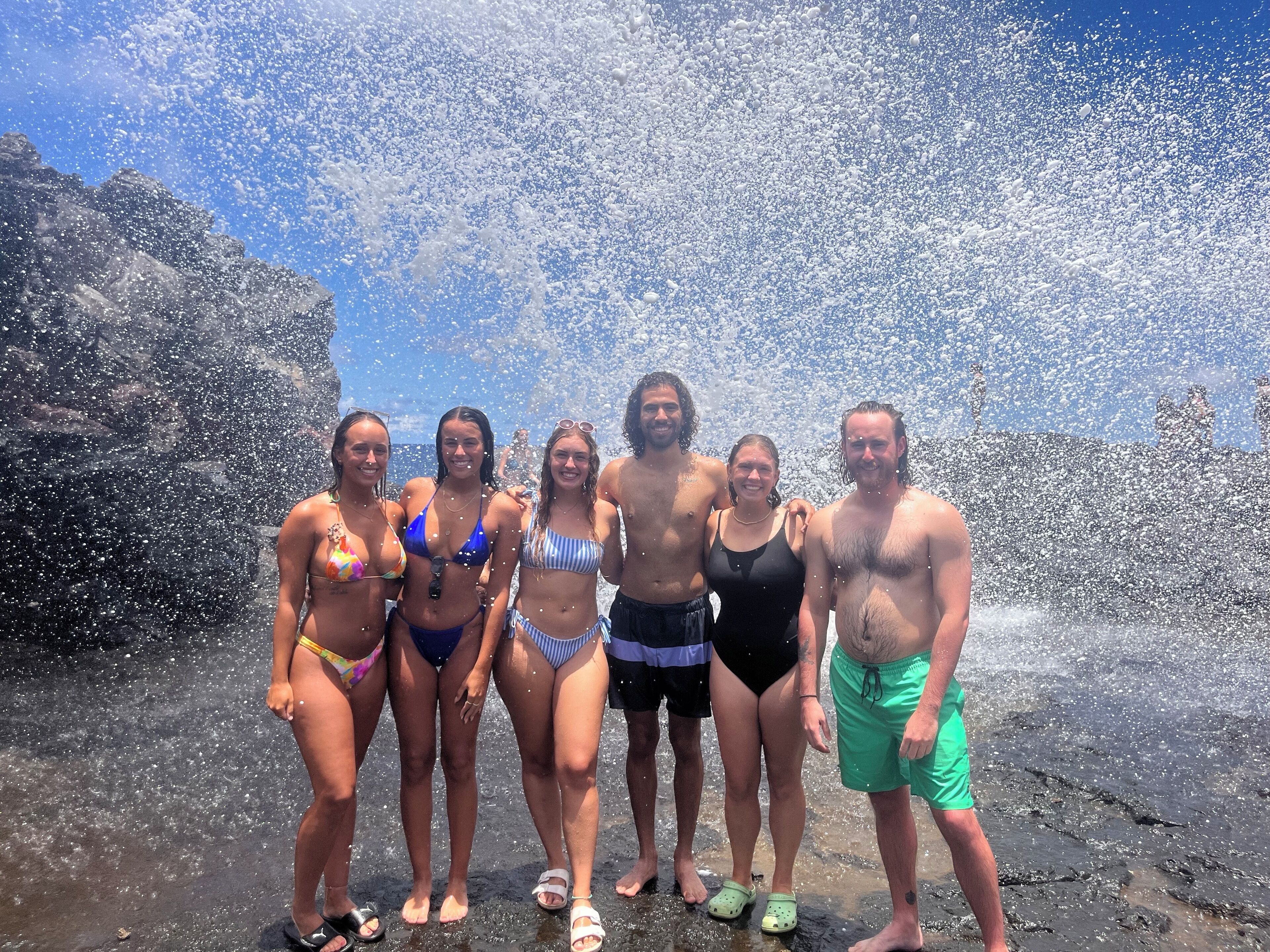 Un grupo de personas de pie en una playa rocosa con olas rompiendo a su alrededor.