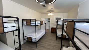 Une chambre de dortoir avec des lits superposés, un ventilateur de plafond et une porte donnant sur une autre pièce.