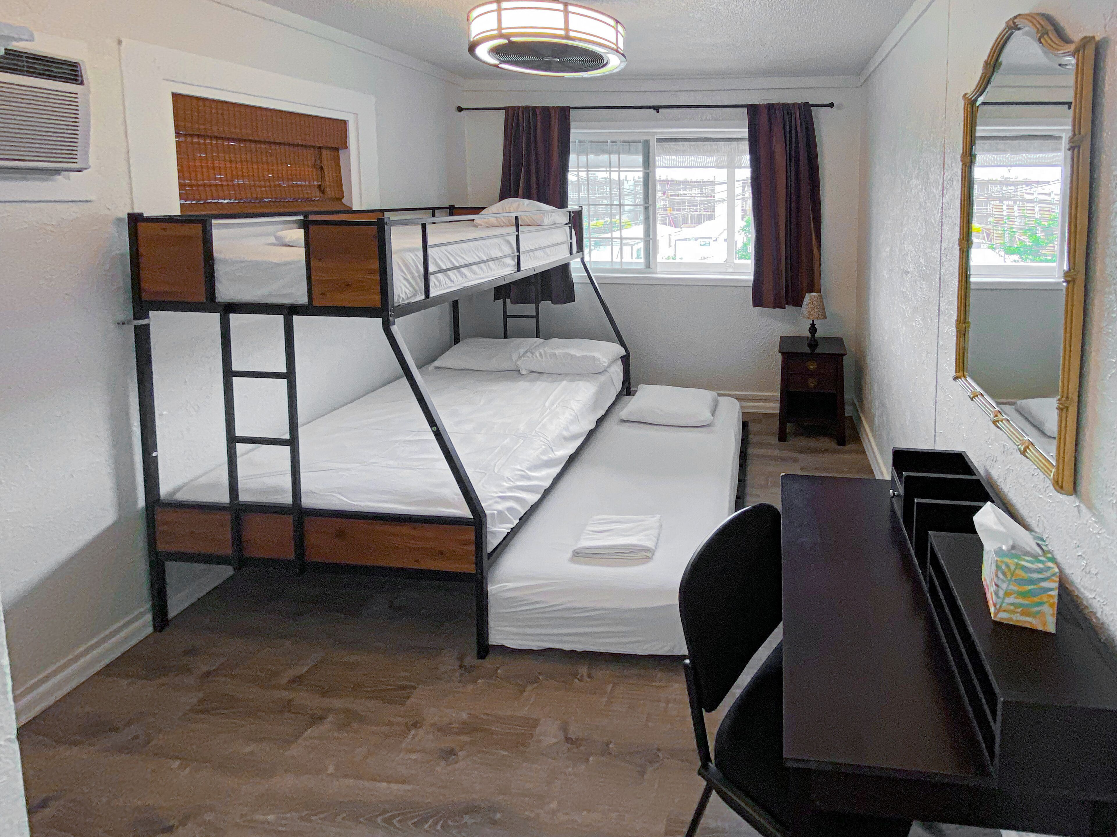 A bunk bed room with a desk and chair, a window with curtains, and a mirror on the wall.