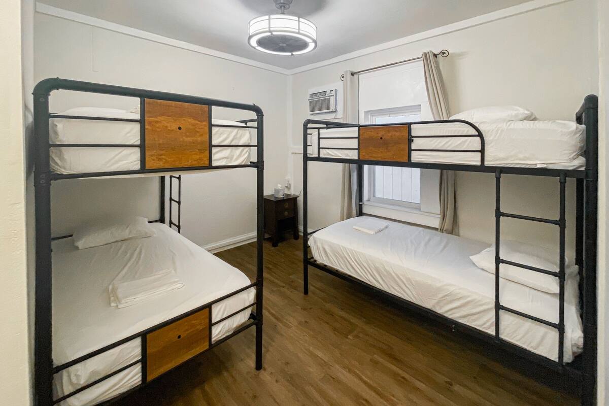 Une chambre avec deux lits superposés, un plancher en bois, un ventilateur de plafond et une fenêtre avec des rideaux.
