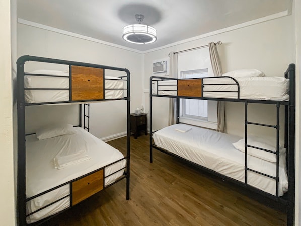 Una habitación con dos literas, suelo de madera, ventilador de techo y una ventana con cortinas.