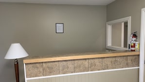 Een kamer met een houten toonbank, een witte lamp, een lijst met een certificaat aan de muur, en een brandblusser.