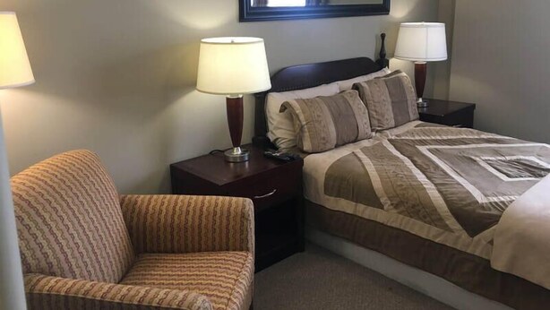 Een hotelkamer met een bed, twee bedlampen, een stoel en een grote spiegel aan de muur.