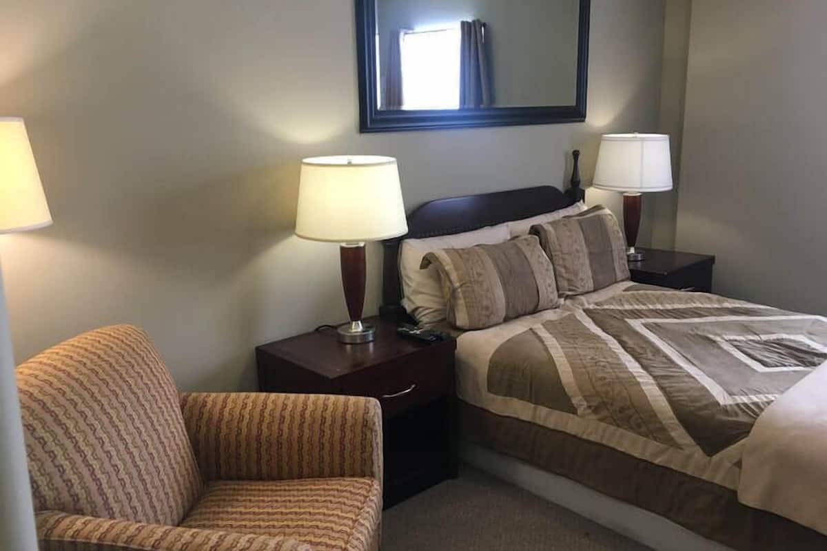 A hotel room with a bed, two bedside lamps, a chair, and a large mirror on the wall.
