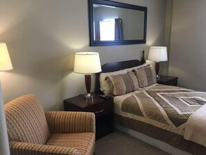 A hotel room with a bed, two bedside lamps, a chair, and a large mirror on the wall.