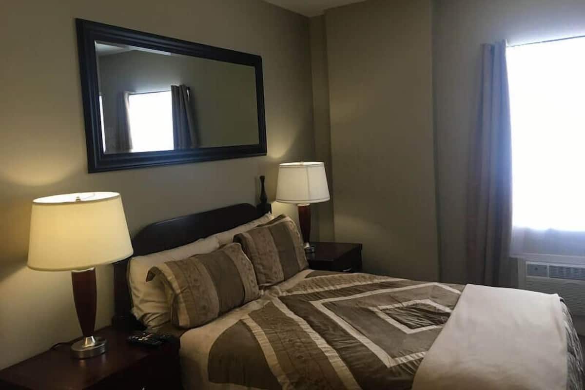 A hotel room with a bed, two bedside lamps, a large mirror, and a window with curtains.
