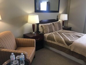 A hotel room with a bed, a chair, a nightstand with lamps, and a mirror on the wall.