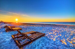 A beach with wooden lounge chairs and a sunset in the background.